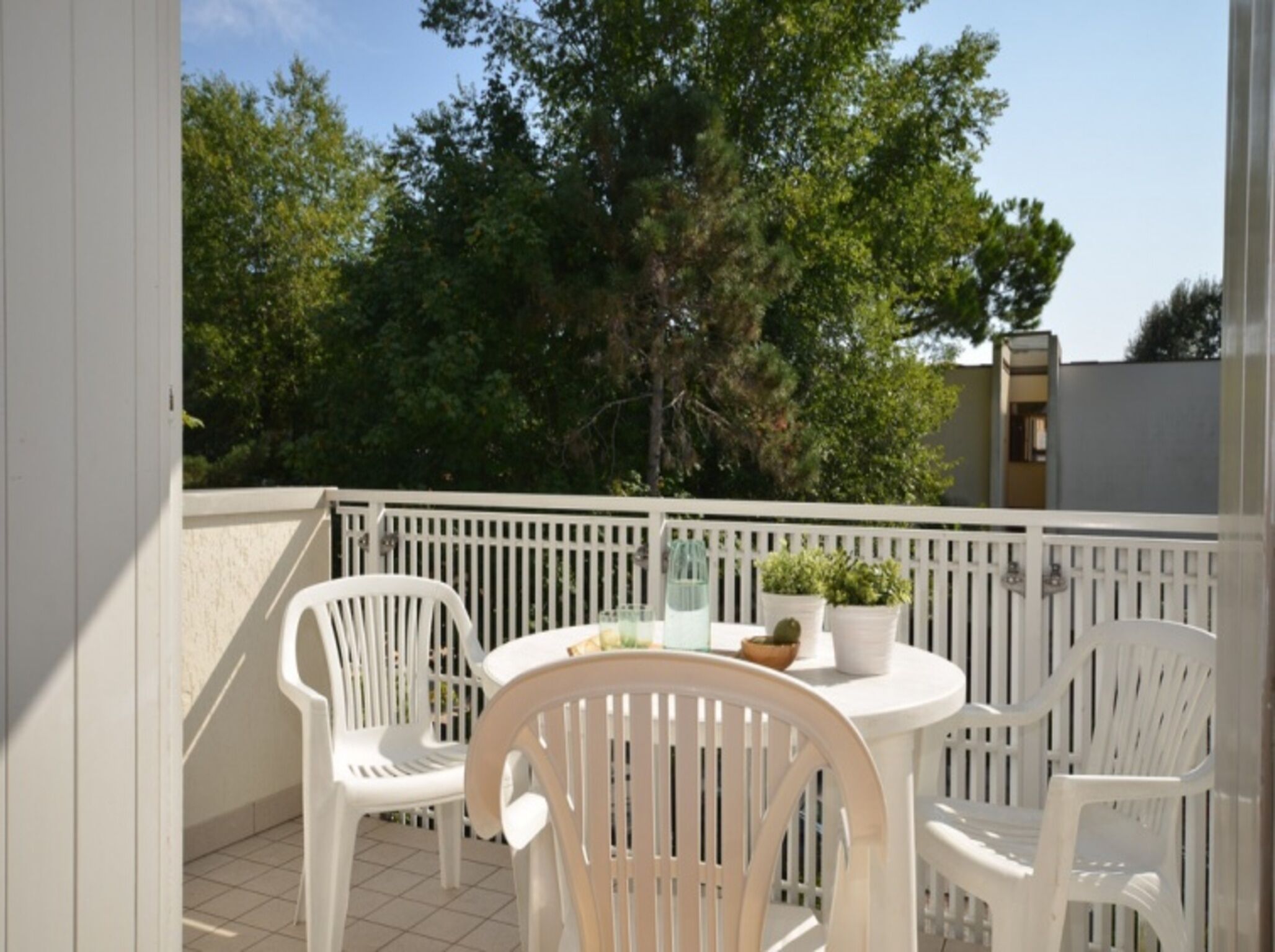 Ein Balkon mit weißen Stühlen und einem Tisch, umgeben von einer weißen Brüstung.