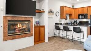 Eine moderne Küche mit Flachbildfernseher, Kamin, Holzausstattung, Mikrowelle und Barhocker.