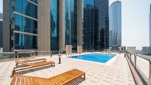 A rooftop pool area with lounge chairs and a view of tall buildings.