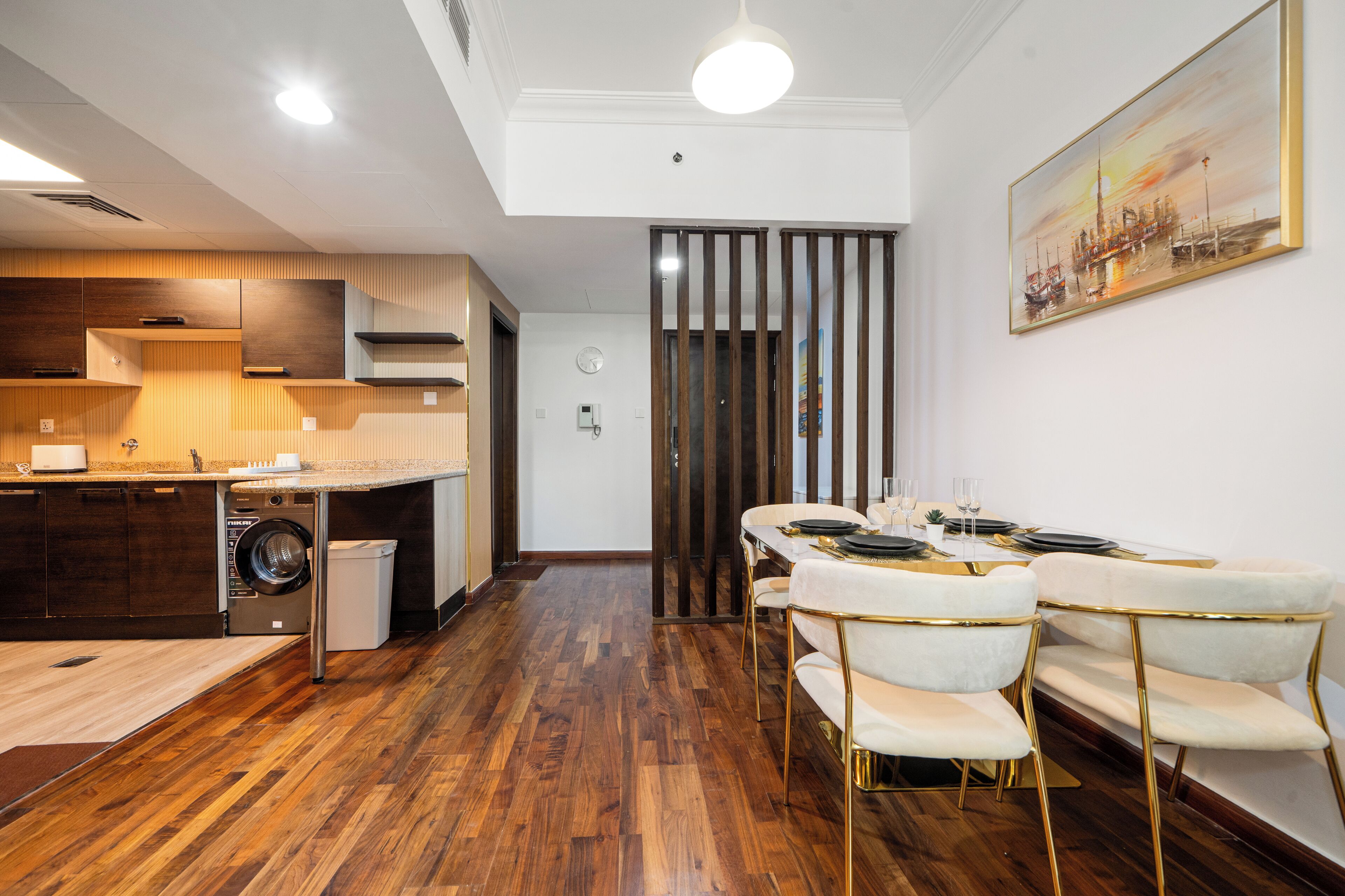 A modern kitchen with wooden cabinets, a built-in washing machine, and a dining area with white chairs and a table set for six.