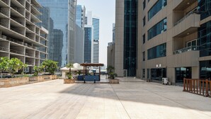 A spacious outdoor area with a wooden pergola, potted plants, and modern buildings in the background.