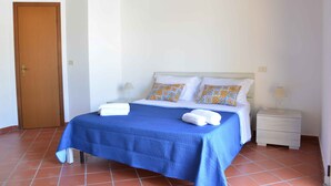 Une chambre à coucher avec un lit, deux tables de chevet, une porte en bois et un sol carrelé.