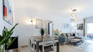 A modern living room with a dining area, a sofa set, and a large window providing natural light.
