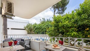 A patio area with a table and chairs, a small table with a cutting board and fruit, and a white railing.