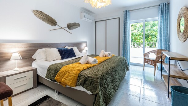 A modern bedroom with a bed, bedside tables, a desk, and a balcony with a view.