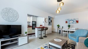A modern living room with a flat-screen TV, a coffee table, a sofa, and a dining area with a table and chairs.