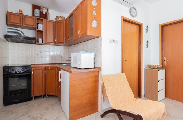 A compact kitchen with wooden cabinets, a stove, a microwave, and a small island.