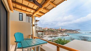 Un balcon avec une table et des chaises, offrant une vue sur la côte, avec des bâtiments et des falaises.
