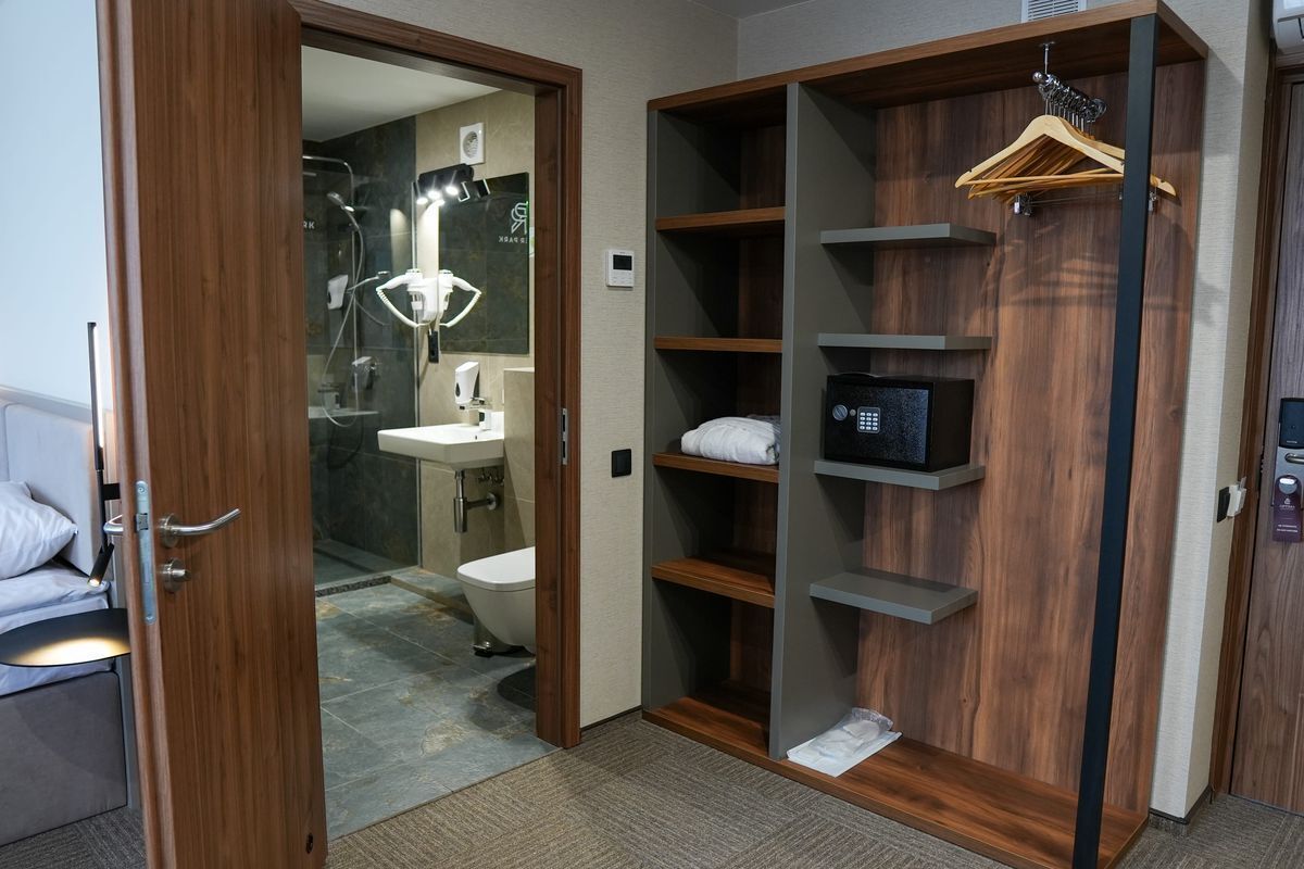Une chambre d’hôtel moderne avec une armoire en bois, une salle de bain comprenant une douche, des toilettes et un lavabo.