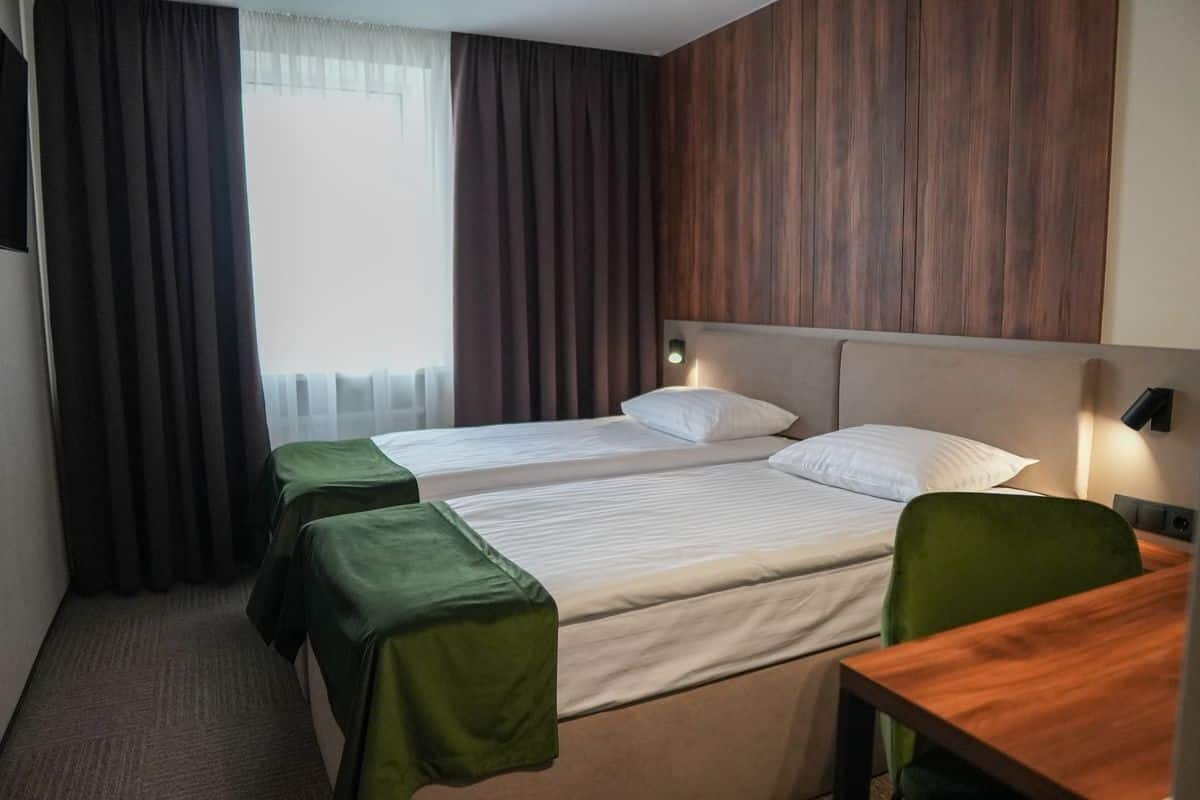 Quarto de hotel com duas camas, cabeceira de madeira, uma escrivaninha e uma cadeira.