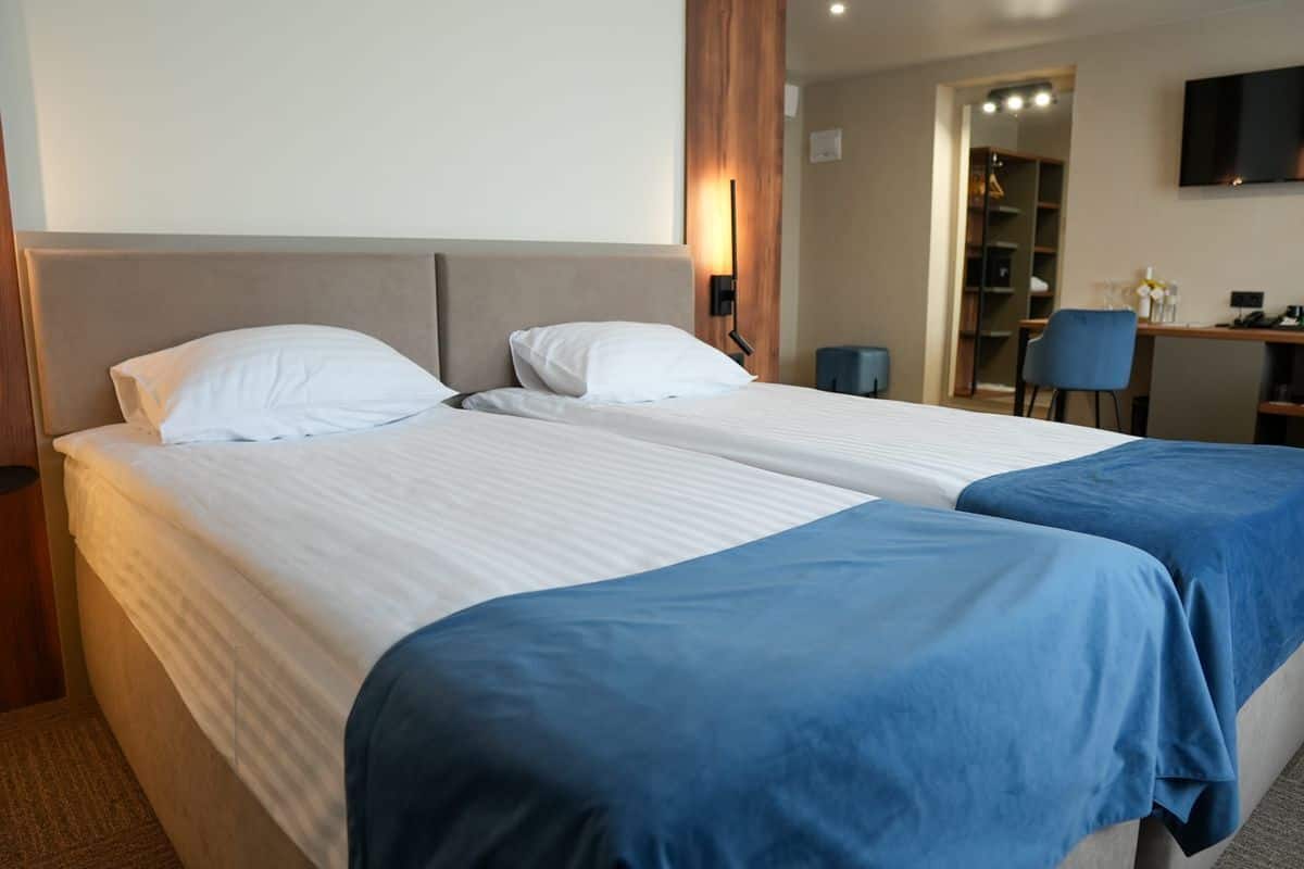 Quarto de hotel com duas camas, uma escrivaninha, uma cadeira e uma televisão.