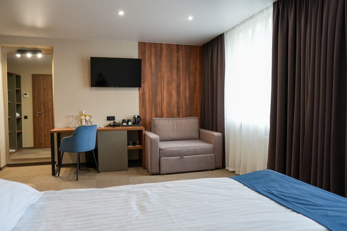 A hotel room with a bed, a desk, a chair, a TV, and a wardrobe.