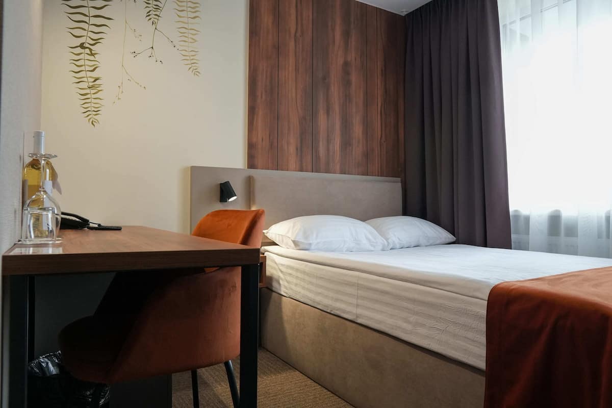 Quarto de hotel com cama, escrivaninha com cadeira, luminária e um objeto decorativo na parede.