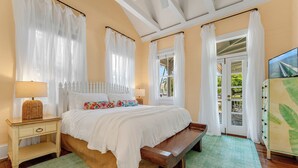 Un dormitorio con cama, mesitas de noche, un banco y vistas al exterior a través de una puerta.