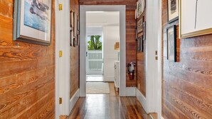 Un pasillo con paredes y puertas de madera que conduce a una habitación con puerta blanca y vistas a la vegetación exterior.
