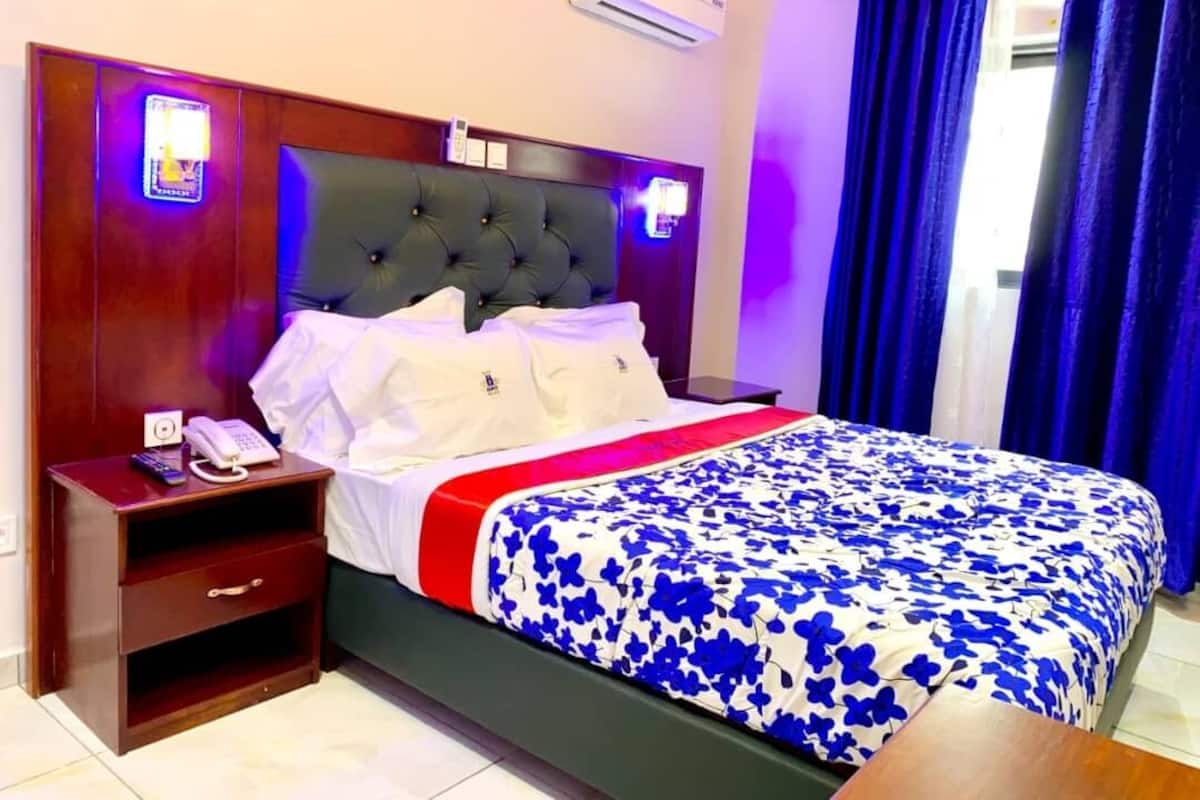 A hotel room with a bed, a bedside table with a phone, and a nightstand.