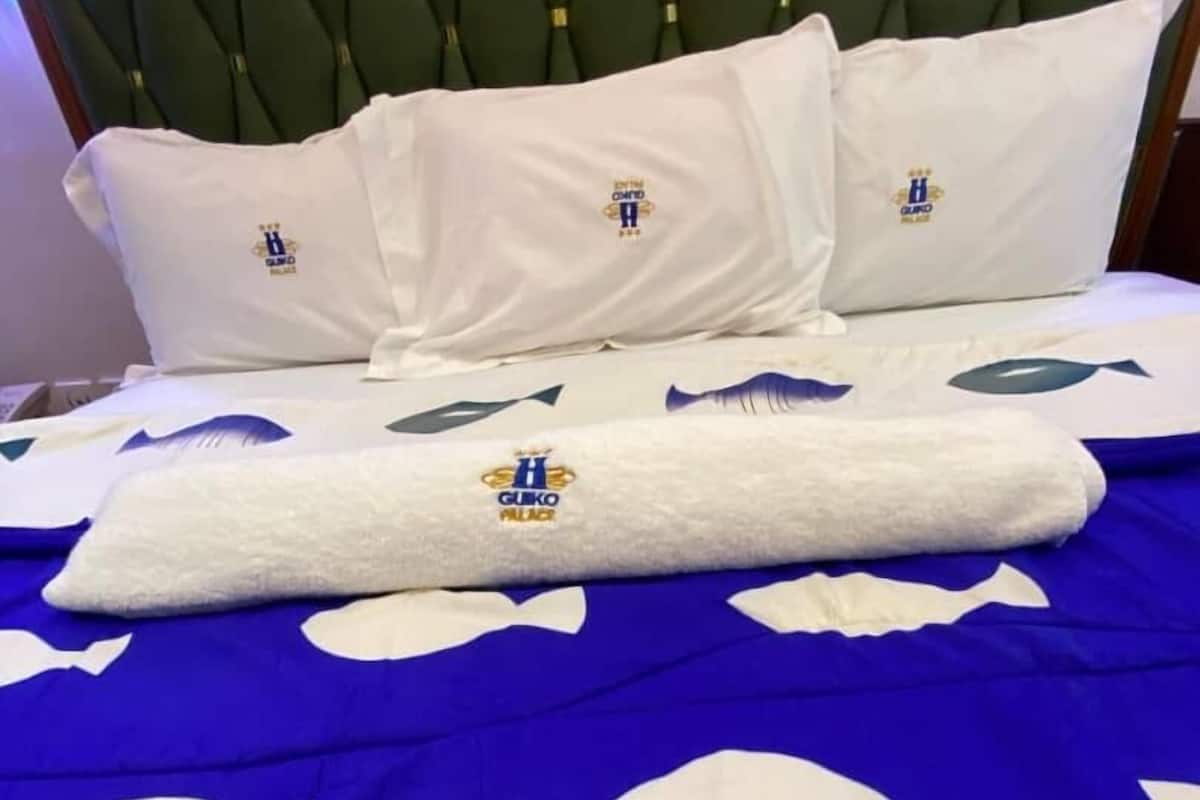 A hotel bed with a blue and white bedspread featuring fish patterns and the 'GUKO PALACE' logo.