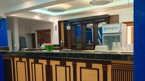 A reception area with a wooden counter, a digital screen, and a sign for INNOVA. - Guiko Palace Hotel  (Douala)