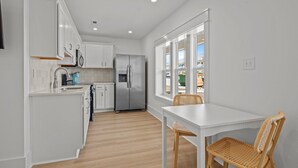 Eine moderne Küche mit weißen Schränken, einem Edelstahlkühlschrank und einem Essbereich mit weißem Tisch und Korbstühlen.