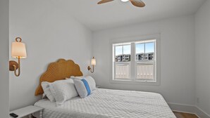 Ein Schlafzimmer mit Bett, Nachttischlampen, einem Fenster mit Jalousien und Blick auf Gebäude.
