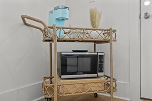 A wicker cart with a microwave and a Keurig coffee maker.