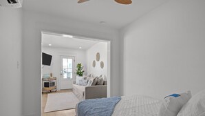 A bedroom with a bed, a bedside table, and a nightstand. There is a door leading to another room.
