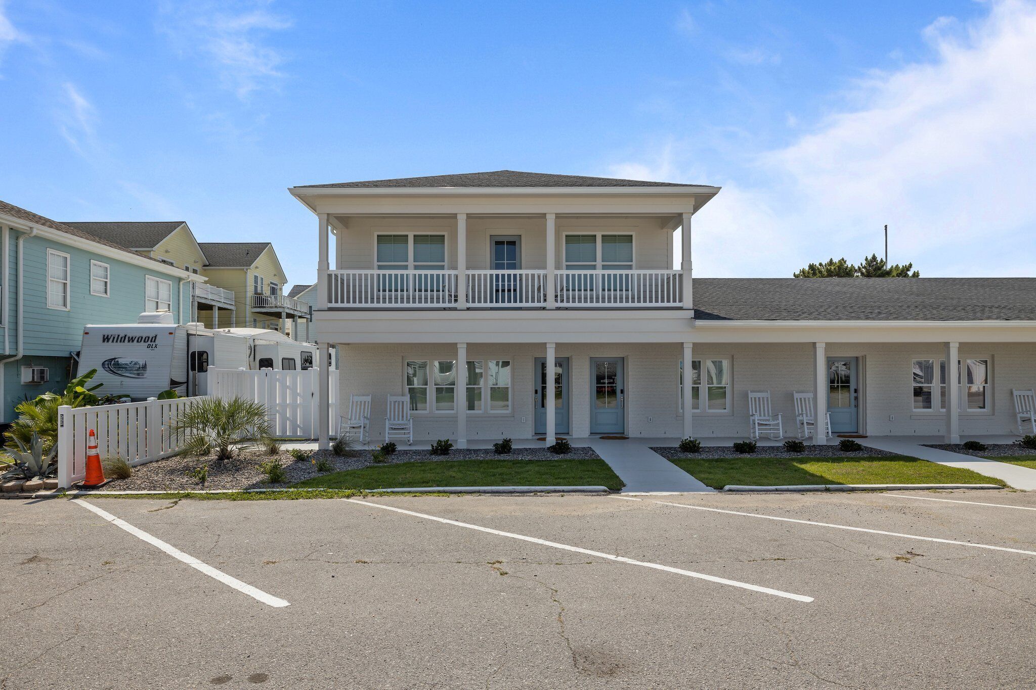 A two-story building with a balcony on the second floor, a parking lot in front, and a white fence with a Wildwood RV parked nearby.