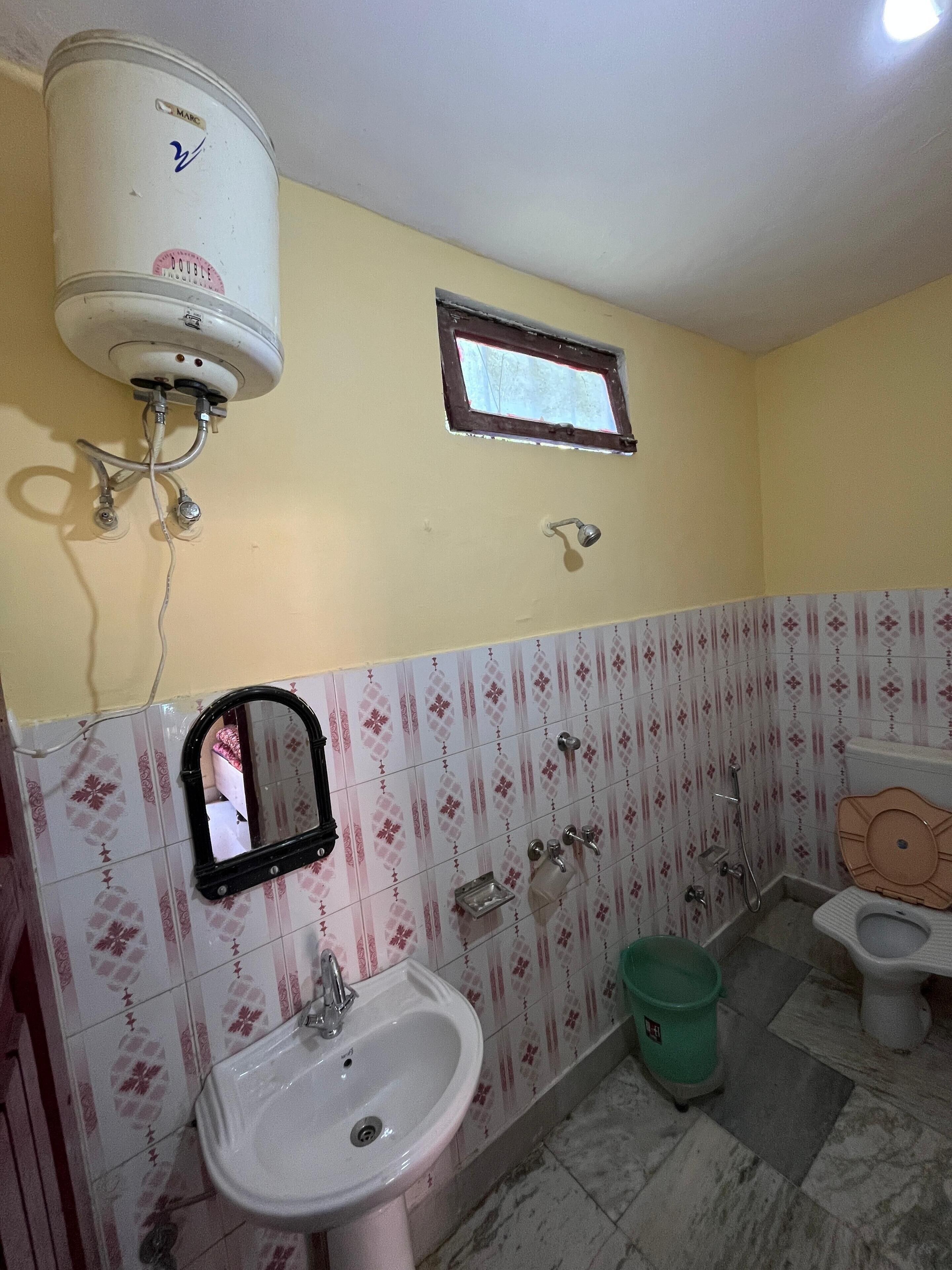 Une salle de bain avec un lavabo blanc, un miroir, des toilettes et une fenêtre.