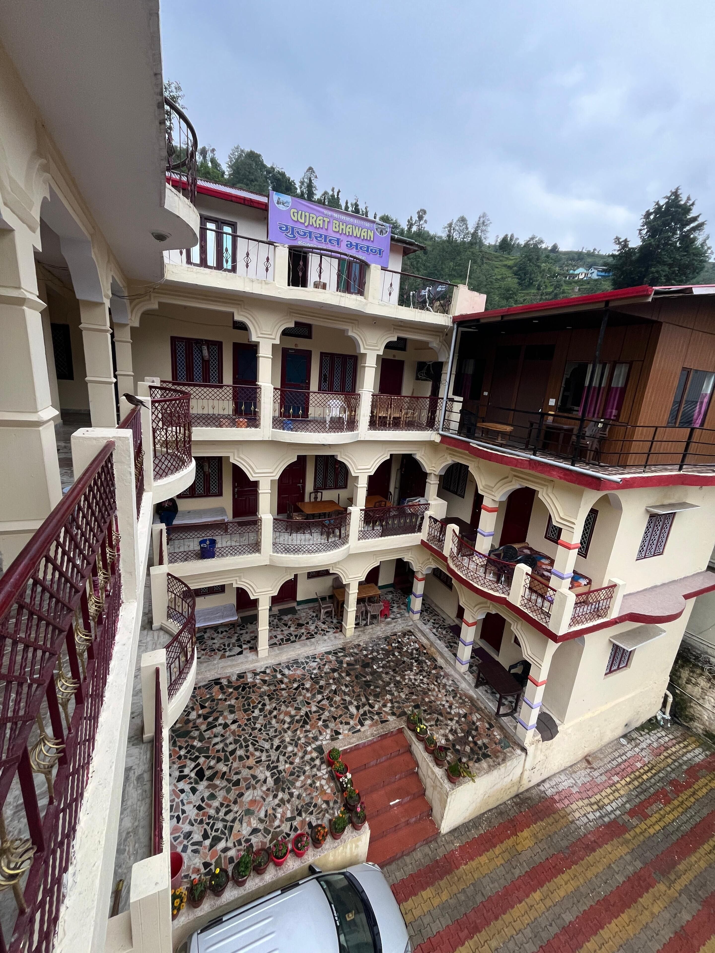 A multi-story building with a sign reading "GUJRAT BHAVAN" and a tiled courtyard with potted plants.