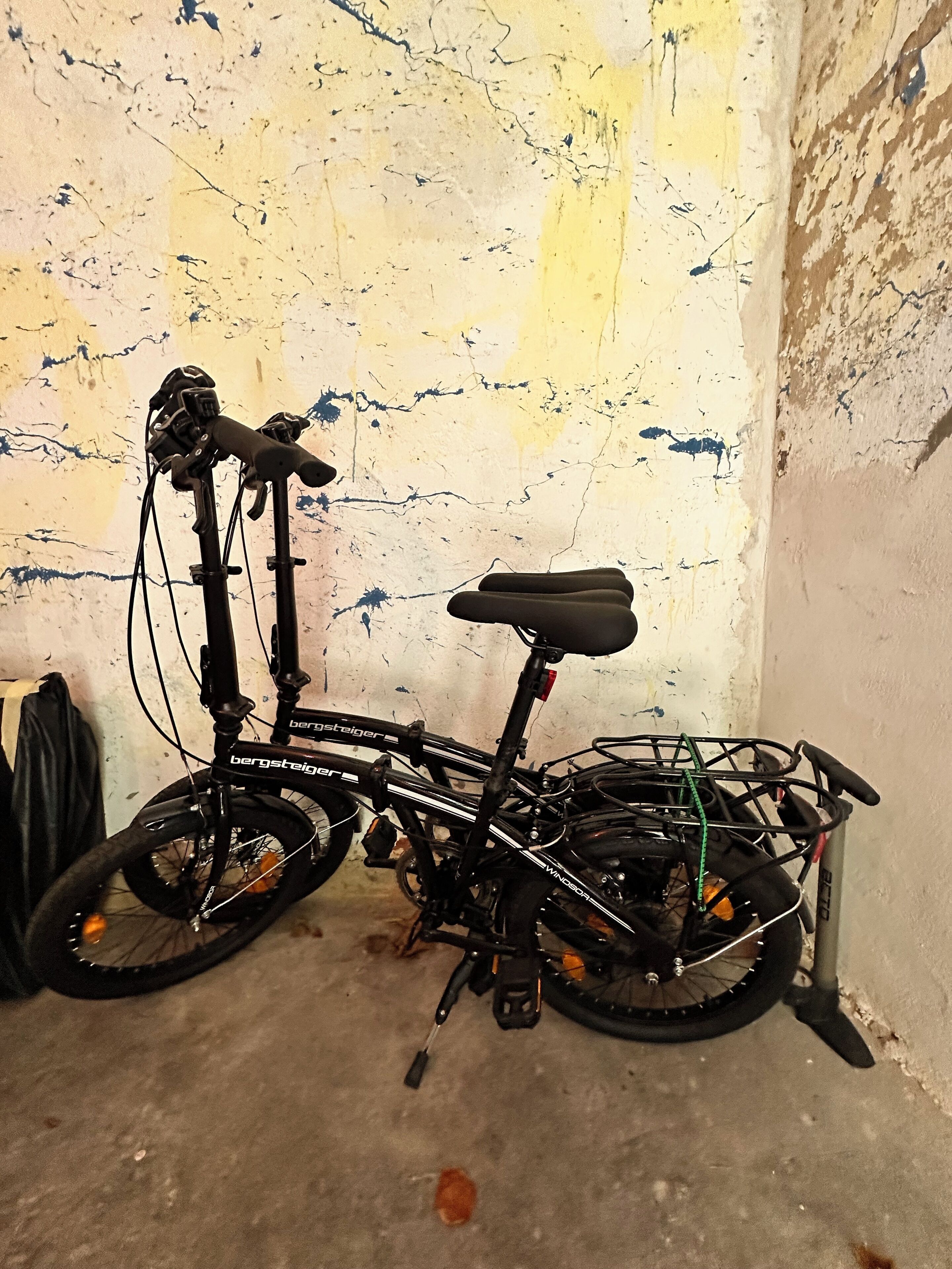 En cykel med kurv foran og bagagebærer bagtil, parkeret op ad en struktureret væg.