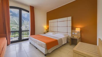 Une chambre d’hôtel comprenant un lit, une table de chevet, une commode, une fenêtre avec des rideaux et une vue sur les montagnes.