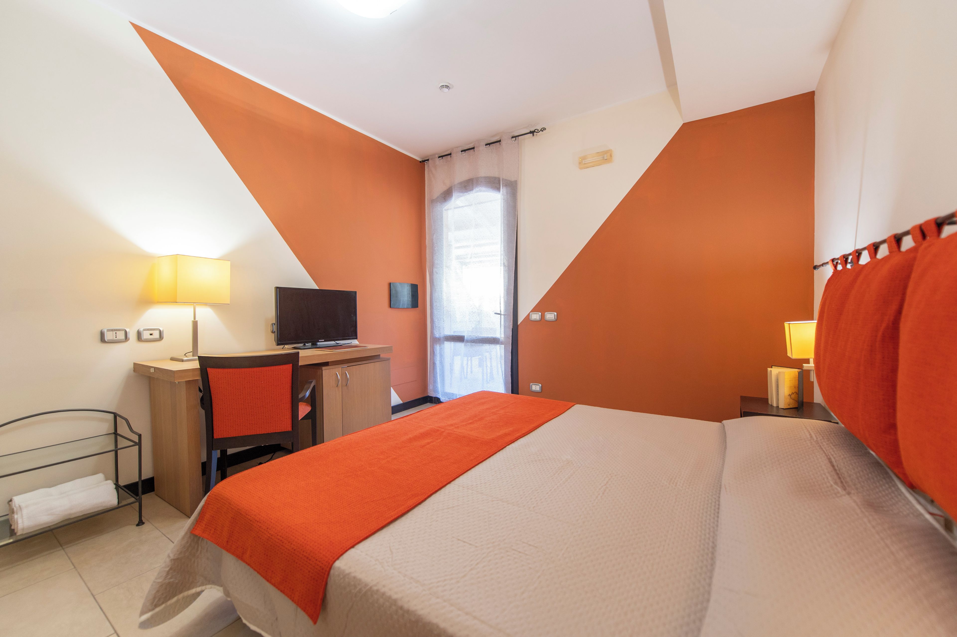 A hotel room with a bed, a desk, a television, and a window.