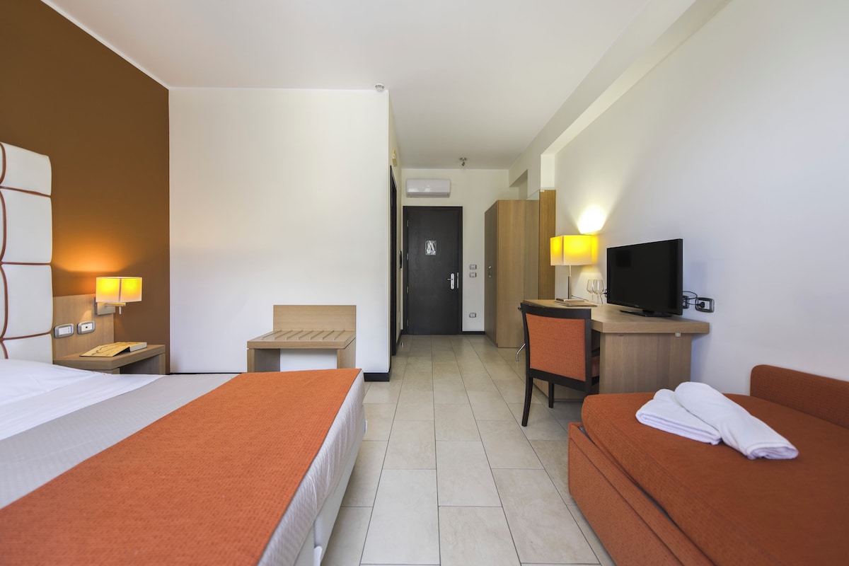 Una habitación de hotel con dos camas, un escritorio, un televisor y un baño visible al fondo.