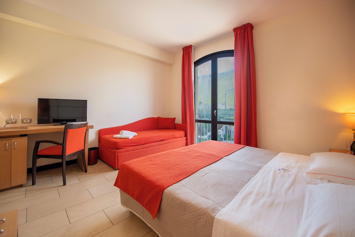 Una habitación de hotel con cama, escritorio, silla, televisor y ventana con cortinas.