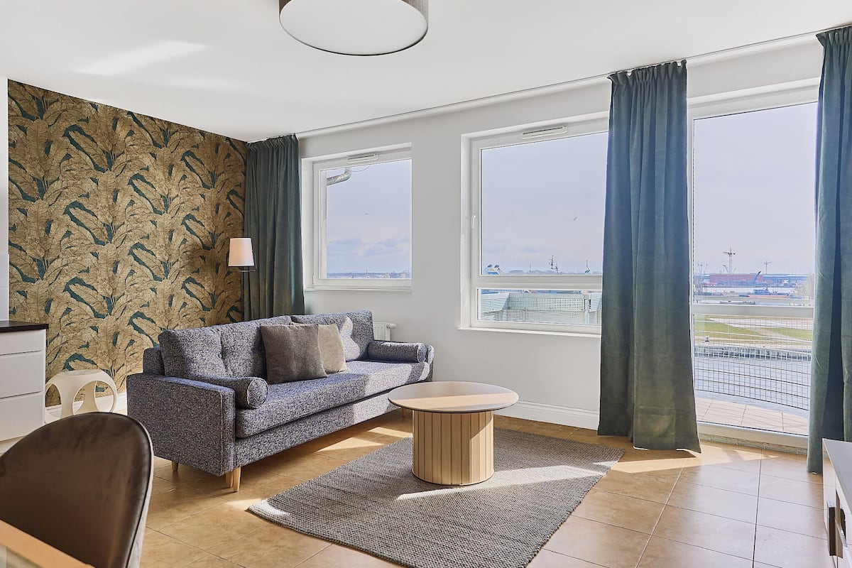 Un salon moderne avec un canapé, une table basse et une vue sur la ville grâce à de grandes fenêtres.