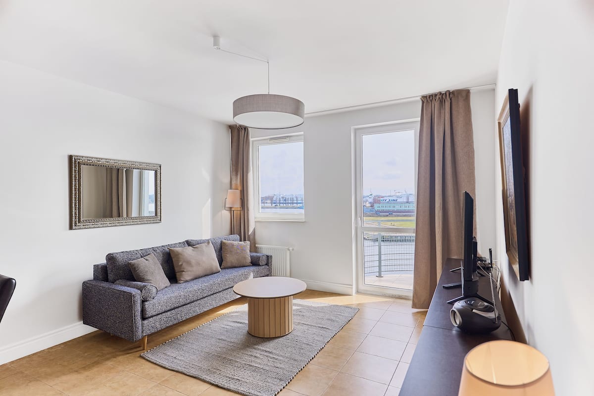 Un salon moderne avec un canapé, une table basse ronde, une lampe et un téléviseur posé sur un meuble.