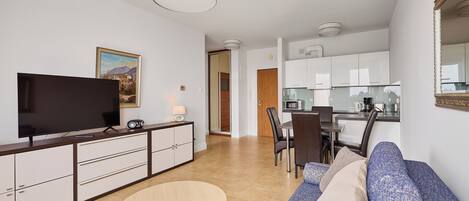 A modern living room with a flat-screen TV, sofa, dining table, and kitchen area.