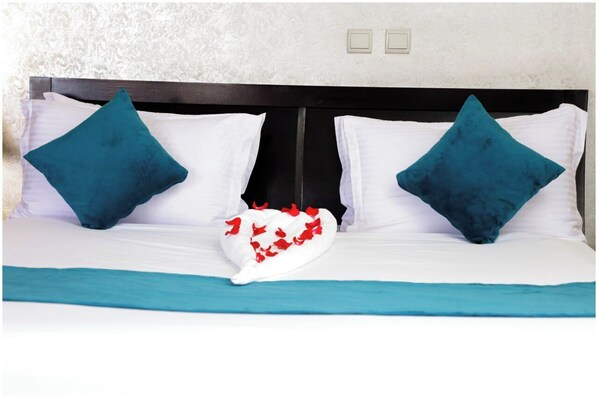 A bed with a teal bedspread, two teal pillows, and a white pillow with red flowers.