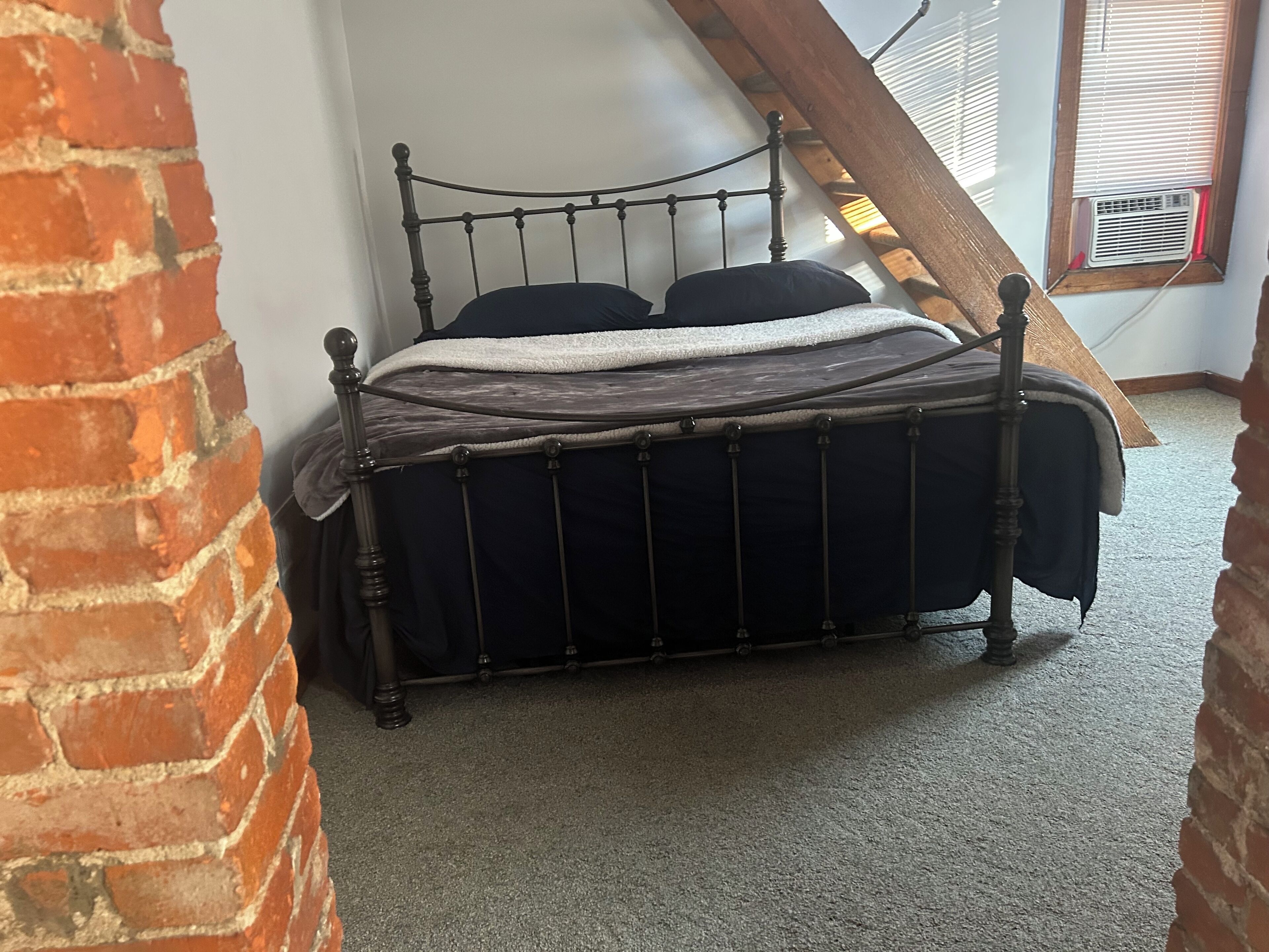 Quarto de canto com parede de tijolos, teto inclinado e janela com persianas.
