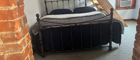 Quarto de canto com parede de tijolos, teto inclinado e janela com persianas.
