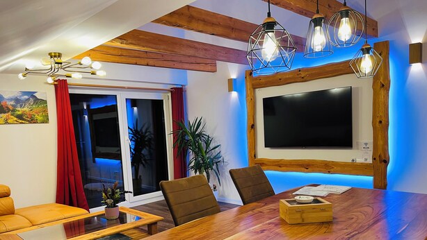 Zona pranzo con tavolo in legno, sedie e televisore fissato al muro.