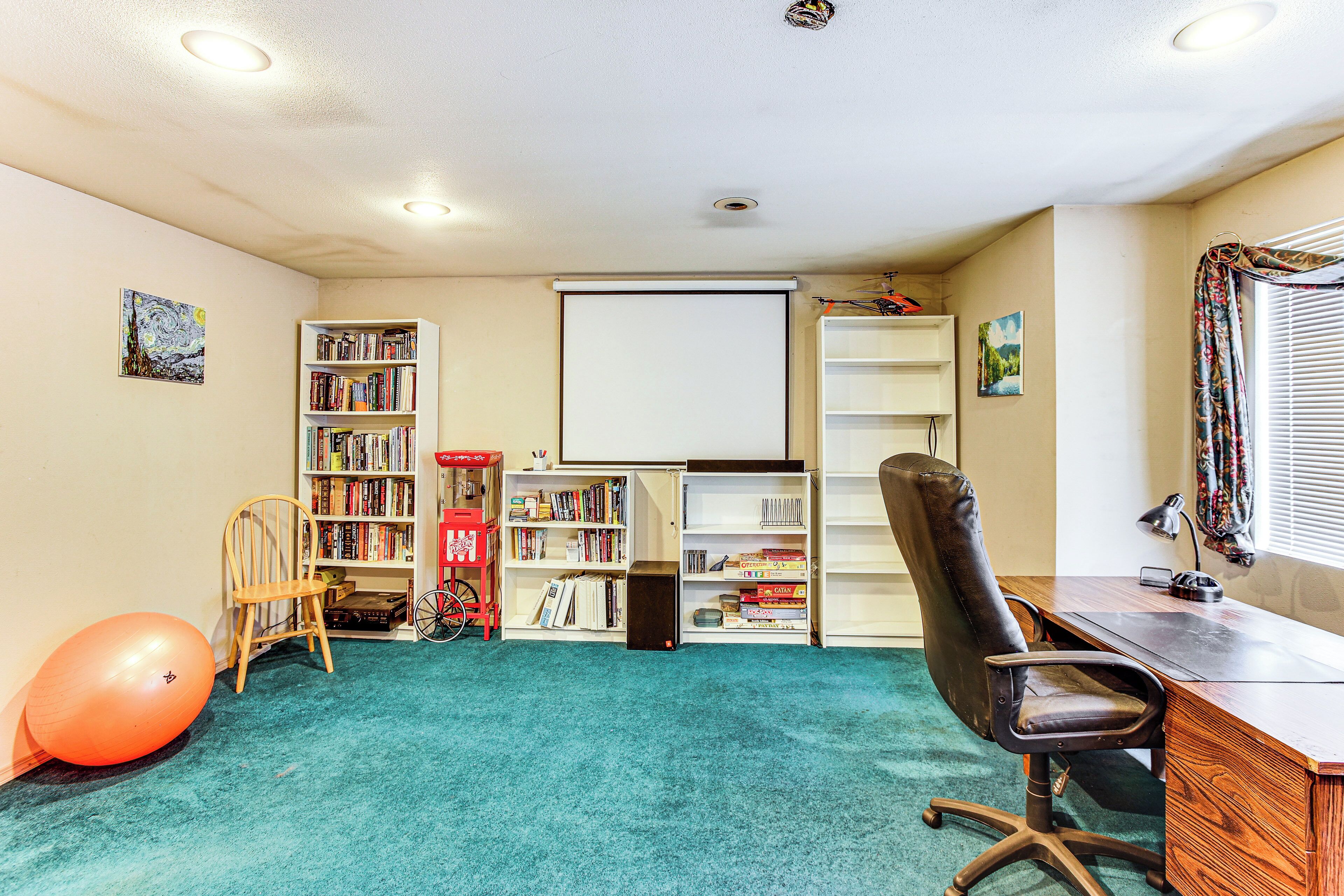 Una habitación con escritorio, dos sillas, una estantería, una pizarra grande y piso alfombrado.