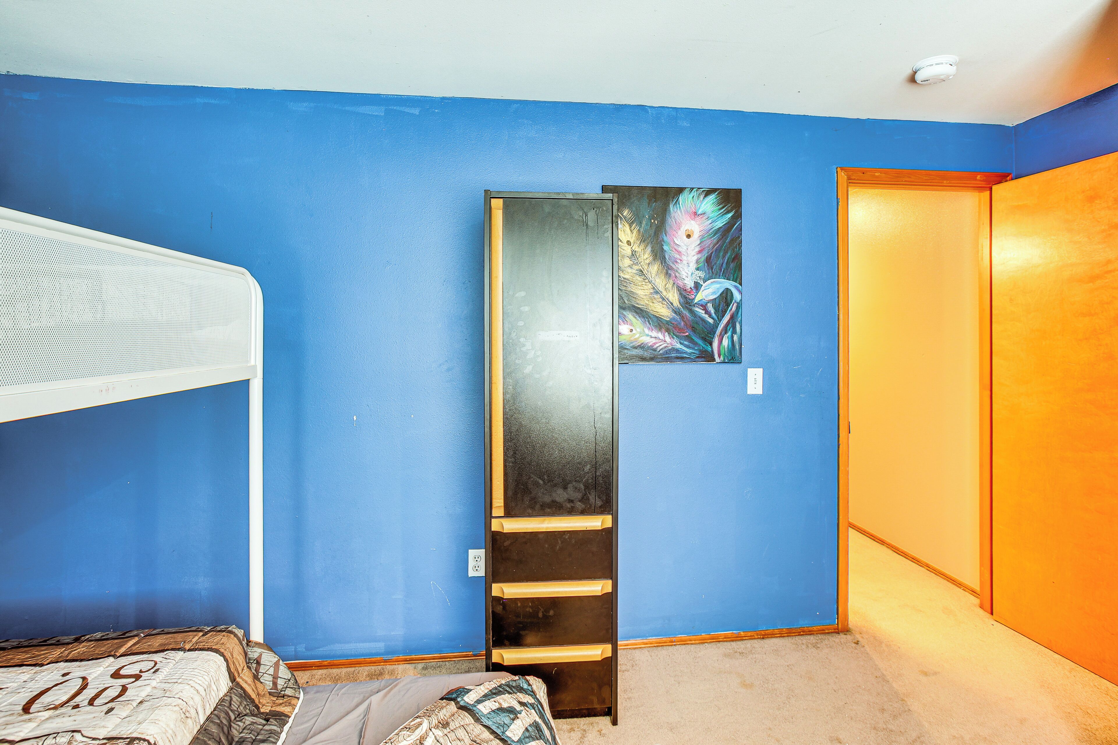 A room with a bunk bed, a wardrobe, and a door with a colorful painting.
