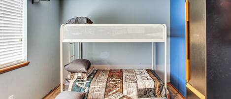 A bunk bed with a quilt, a window with blinds, and a dark-colored wardrobe.