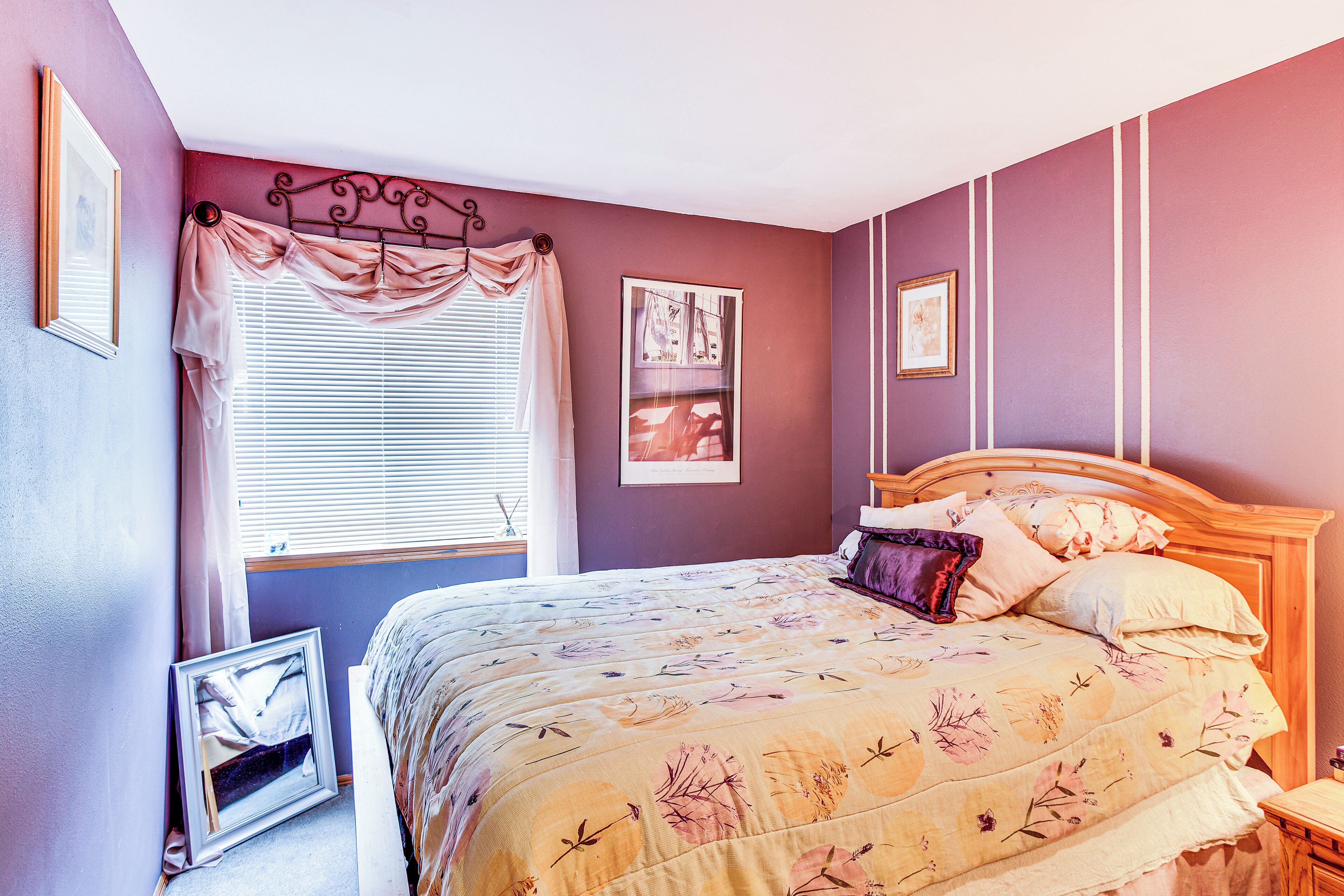 Une chambre à coucher avec un lit, une fenêtre avec des rideaux et des tableaux encadrés accrochés au mur.