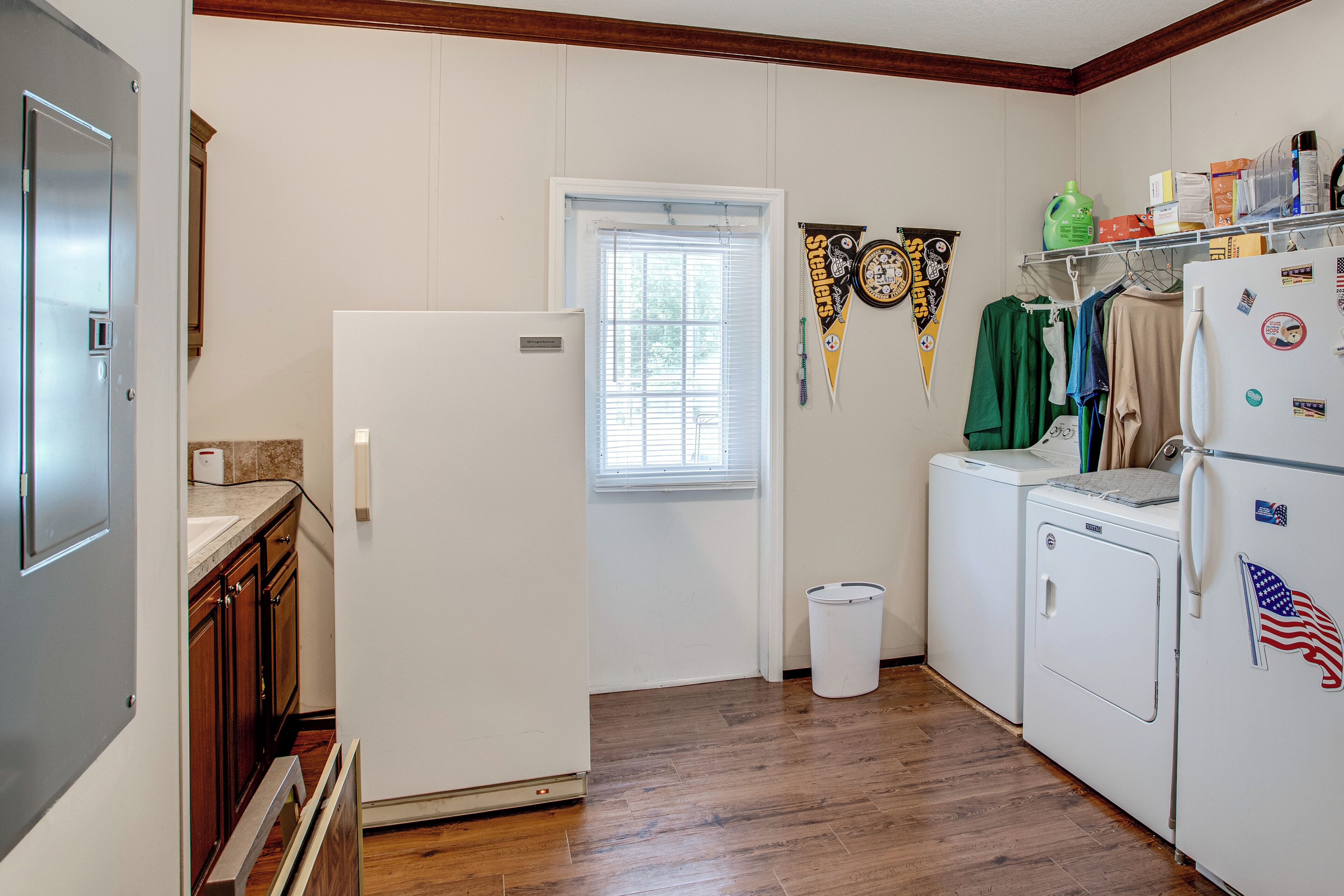 Cocina compacta con refrigerador, lavadora y secadora, armarios de madera y ventana con persianas.