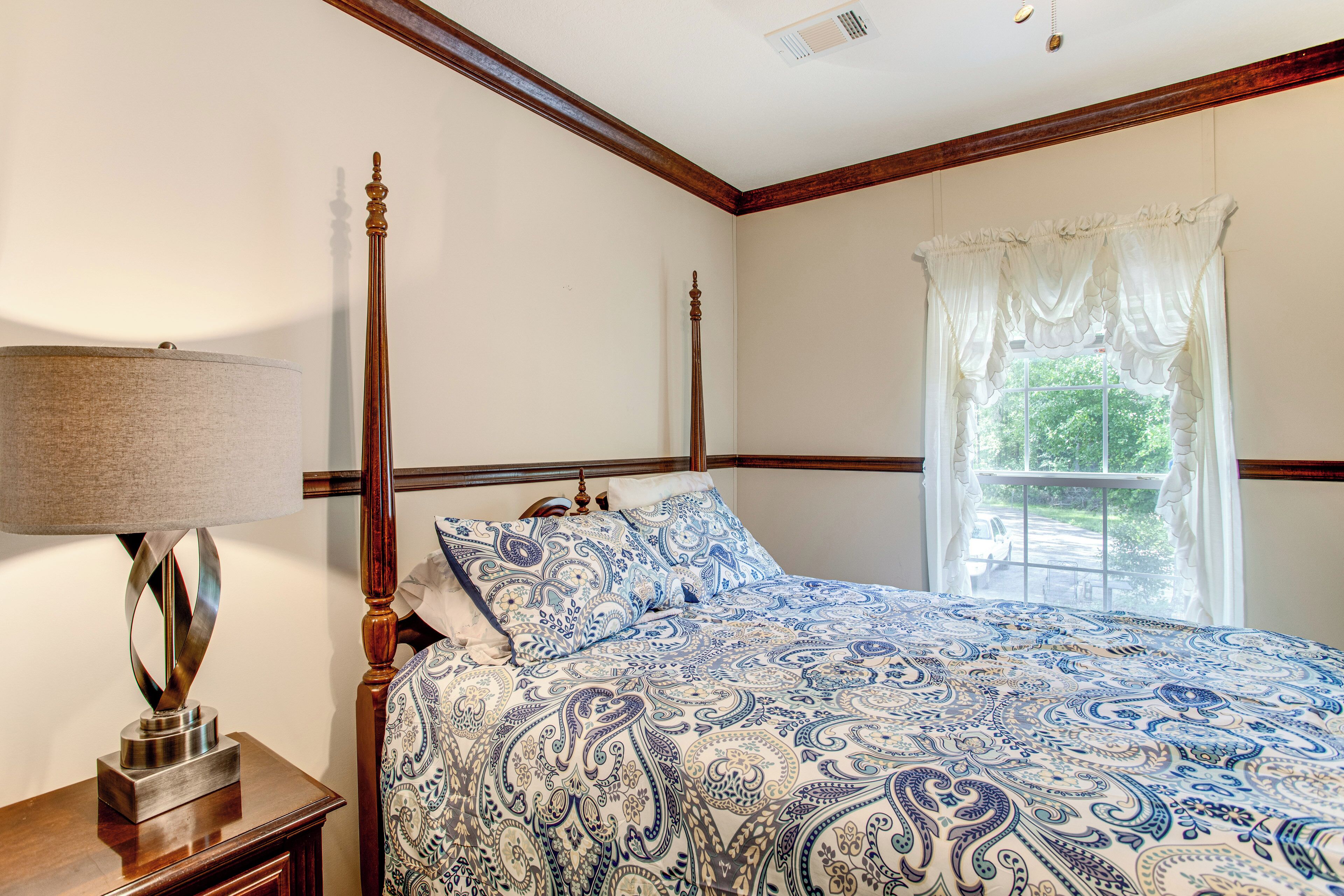 A bedroom with a four-poster bed, a bedside table with a lamp, and a window with curtains.