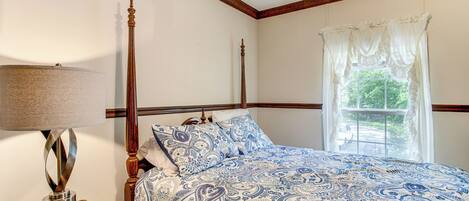 A bedroom with a four-poster bed, a bedside table with a lamp, and a window with curtains.