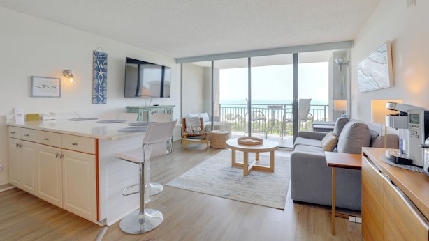 Ein modernes Wohnzimmer mit einer Couch, einem Couchtisch und einem Fernseher. Es gibt einen Balkon mit Meerblick.