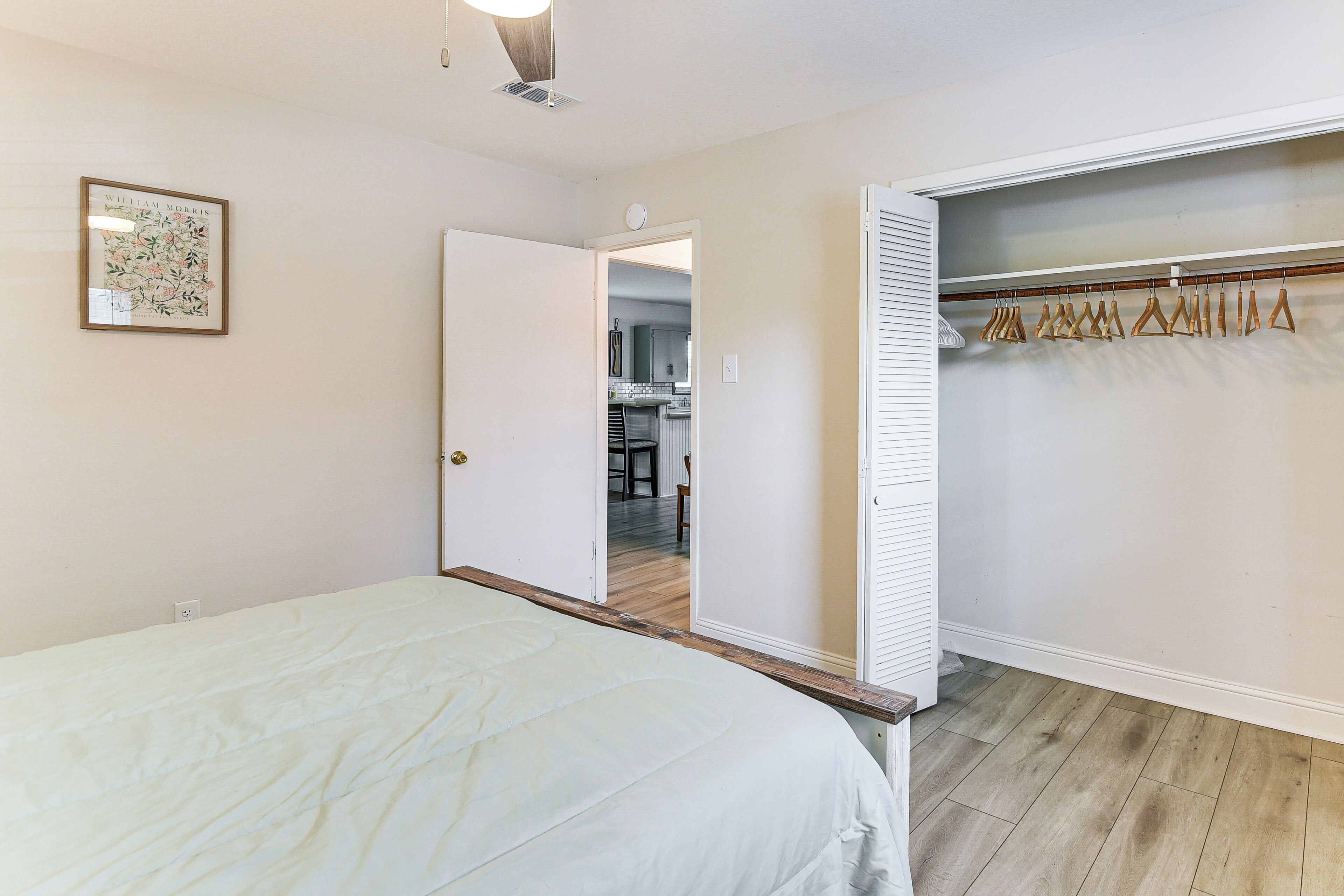 A bedroom with a bed, a closet with hangers, and a door leading to a kitchen.